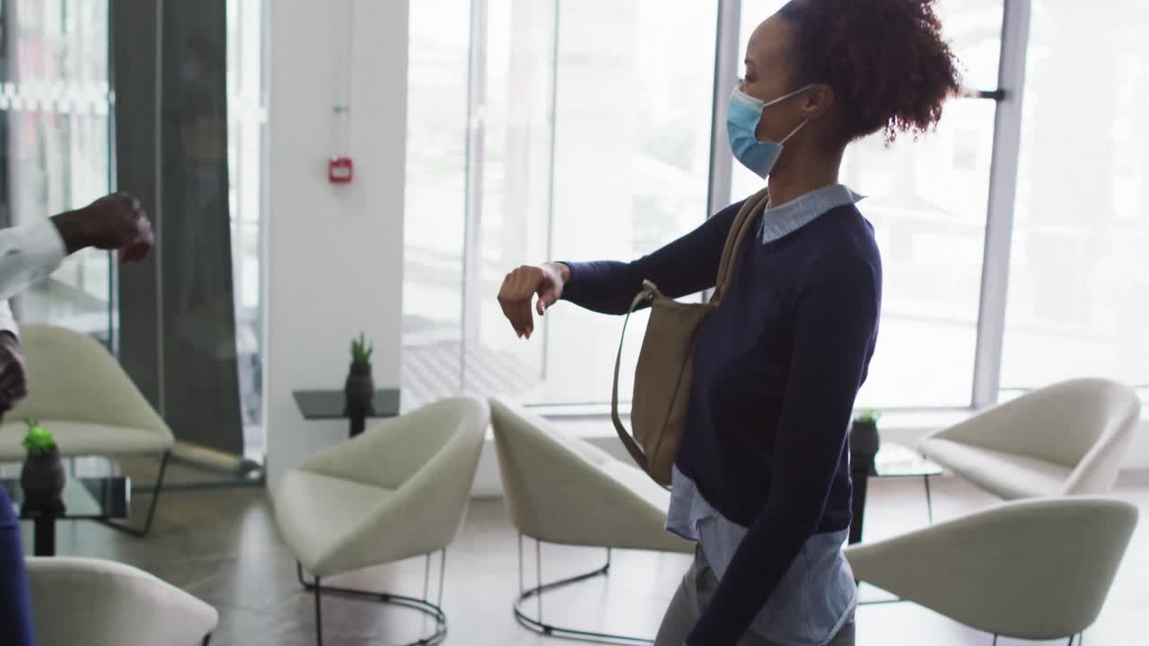 различные мужские и женские деловые коллеги в масках приветствуют, касаясь локтей в офисе