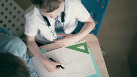 high-angle shot children perform school homework sitting at a table in a notebook get tired yawn