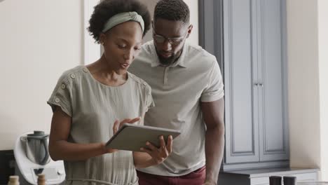 Happy-african-american-couple-using-tablet-in-ktichen-in-slow-motion