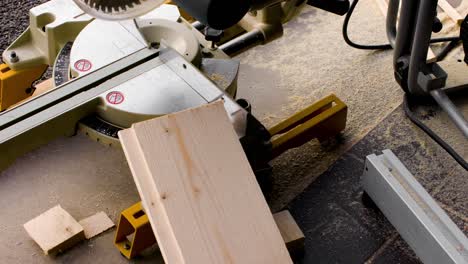 pan over a mitre saw with pieces of cut wood and sawdust around it in 4k