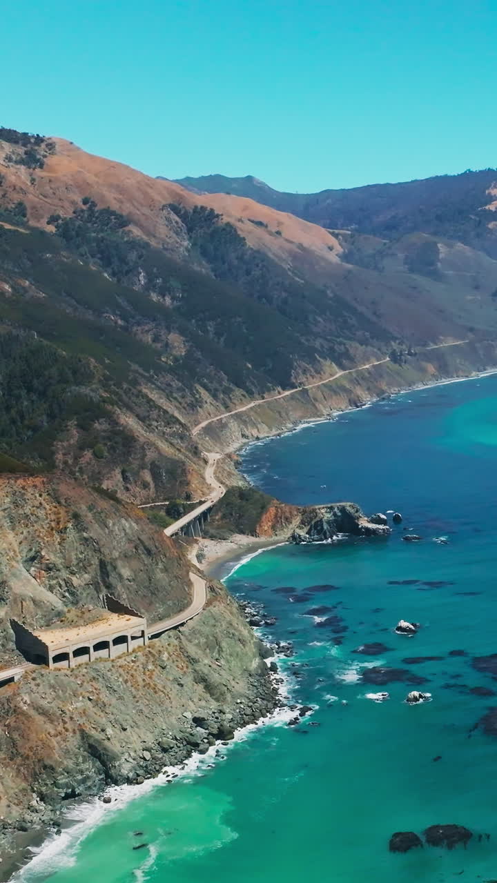 Breath-taking scenery of mountains with some greenery growing on. Turquoise ocean washing the rocky shore. Aerial view. Vertical video