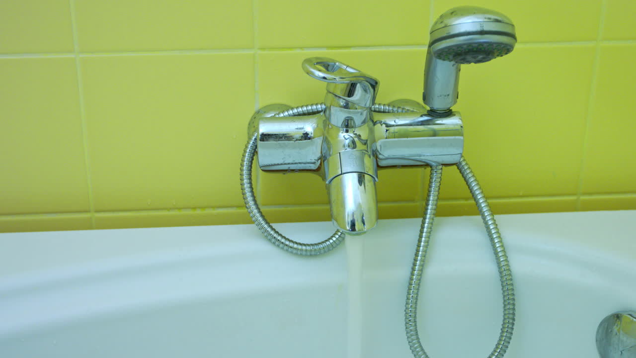 Closeup of a faucet over a bathtub that fills the bathtub with warm water before bathing