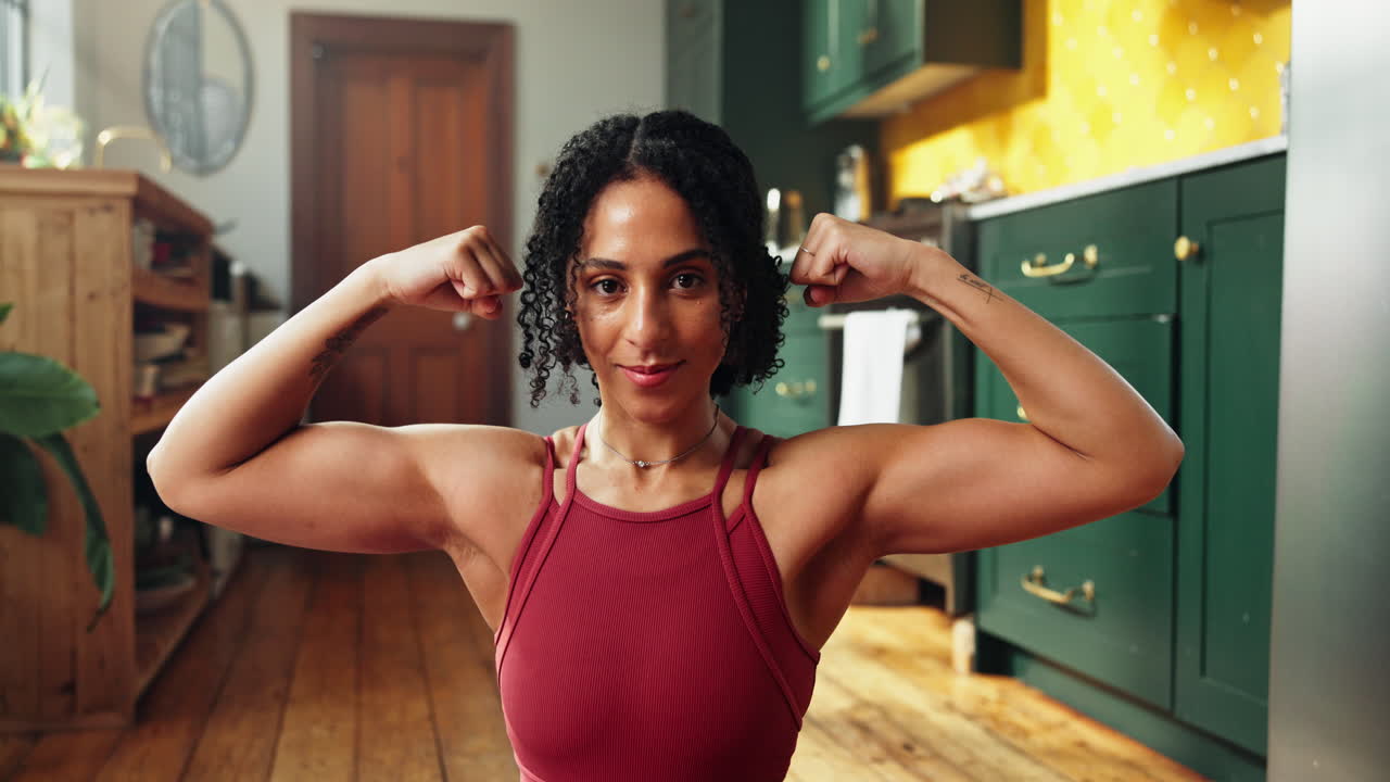Young Woman Flexing Biceps and Smiling Confidently at Home