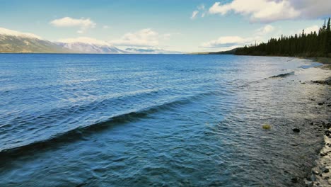 waves washing on shore of atlin lake with white peak mountain in background, british columbia, canada