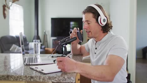 hombre caucásico enfocado con auriculares, grabando y tomando notas