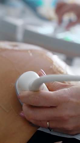 doctor's hand moving the device by the big gelled belly of pregnant. ultrasonic examination of pregnancy development. vertical video