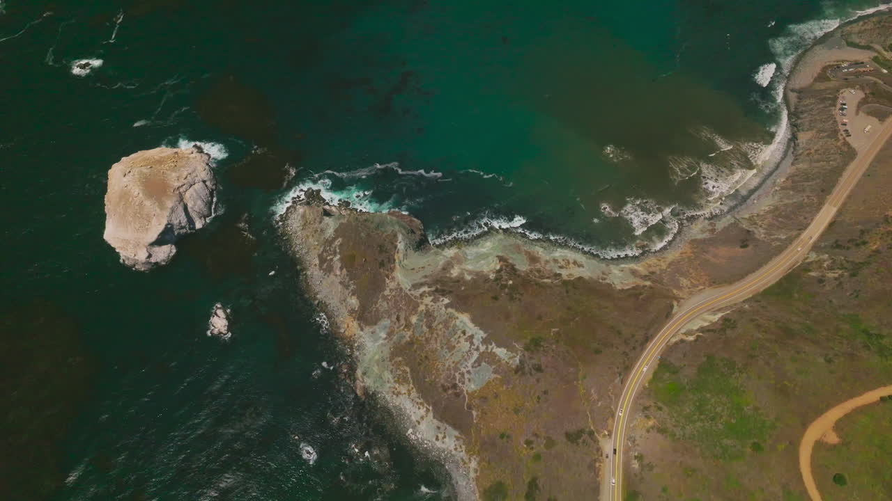 Mountainous landscape crossed by roads with moving cars. Sea-green water of Pacific ocean washing the bare rocks. Sunny day footage.