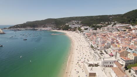 aerial backwards view of long and beautiful beach with its bay in sesimbra. portugal. real time