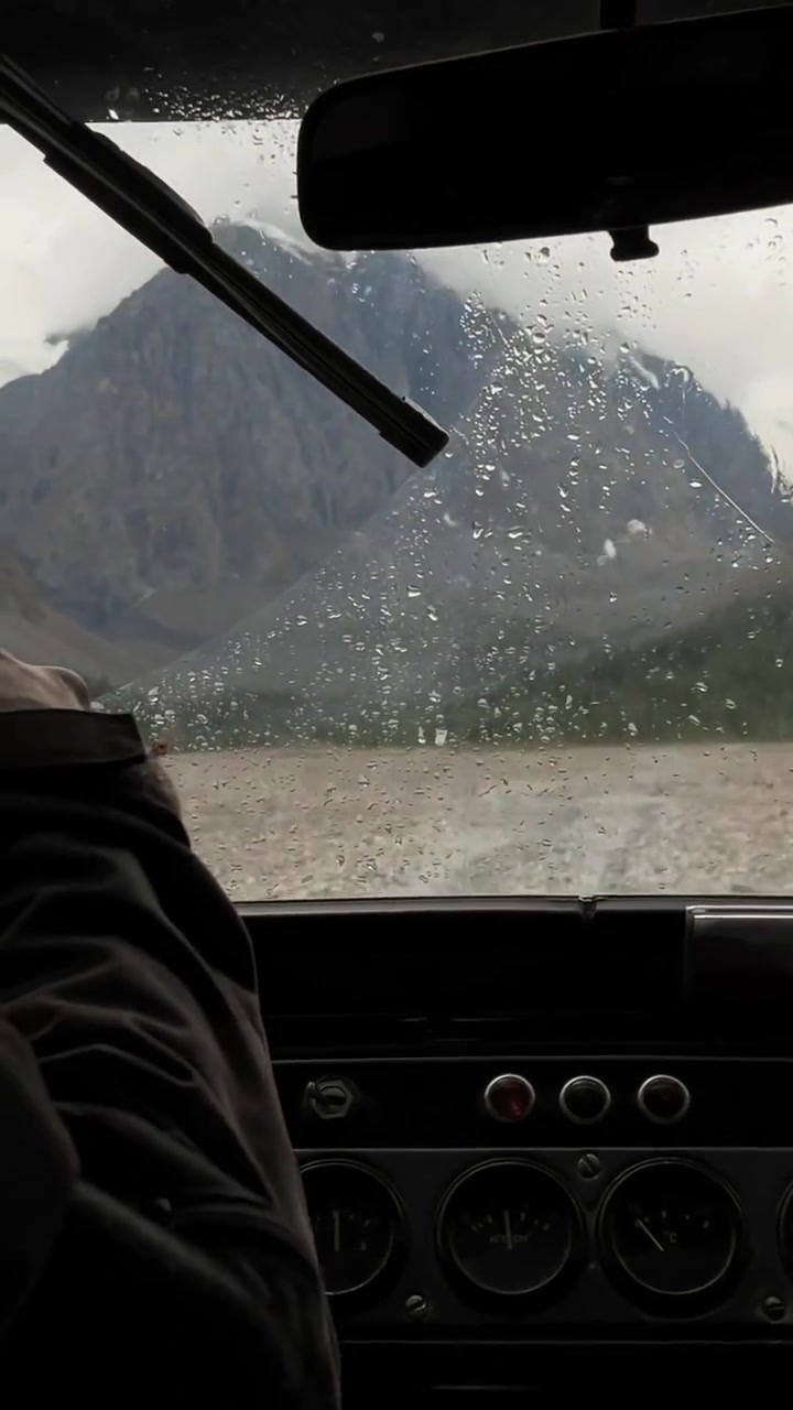 Vista dall'interno di un'auto durante tempo piovoso, gocce d'acqua sul parabrezza e tergicristallo in movimento, paesaggio di montagne e valle fluviale nella Valle di Akturu, Altai, Russia.