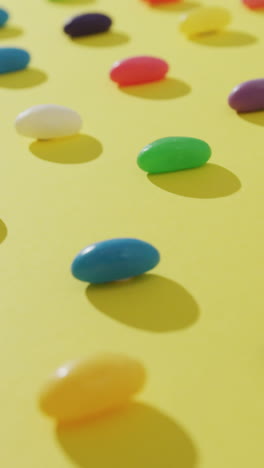 video of overhead view of rows of multi coloured sweets over yellow background