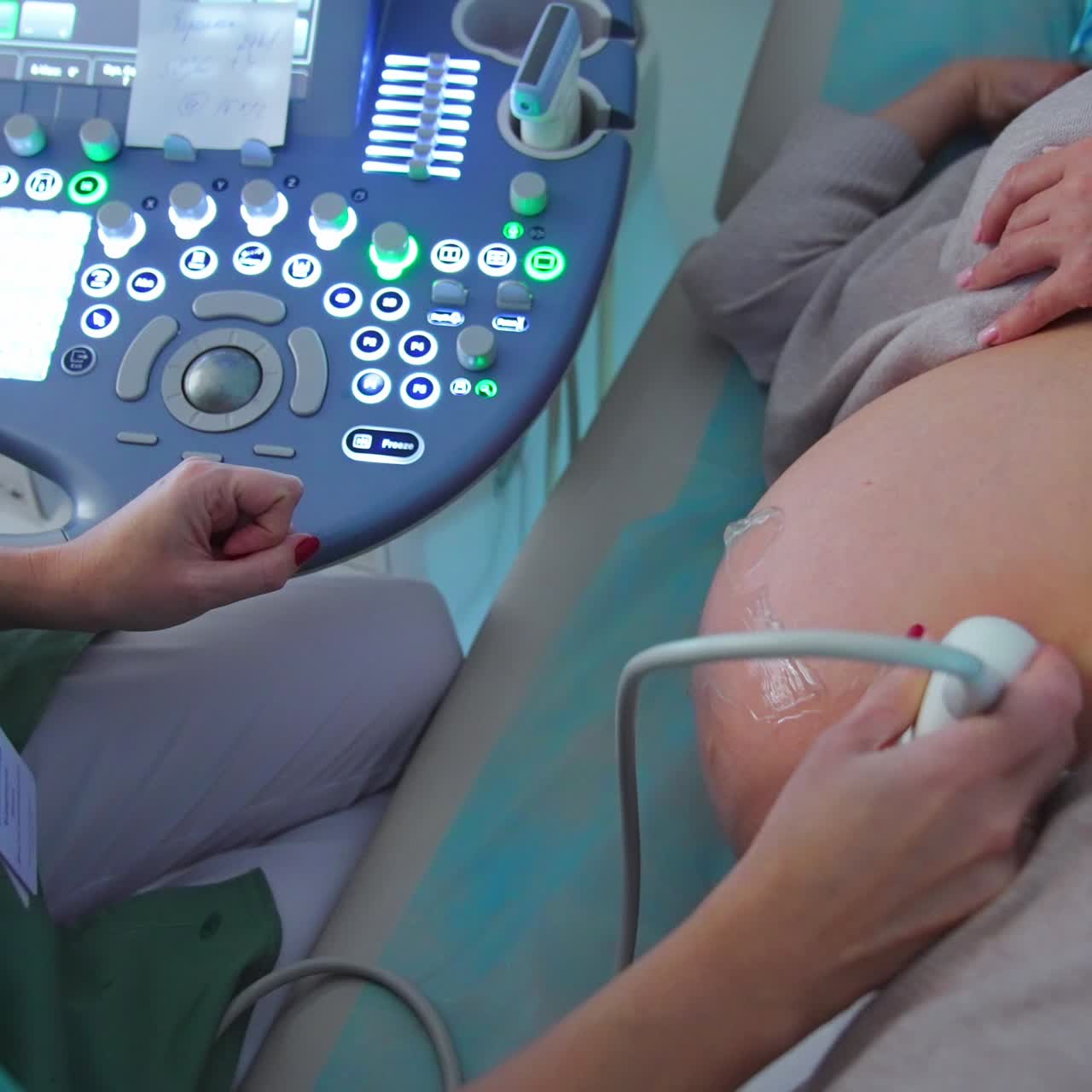 Pregnant lady lies on the couch on her side. Obstetrician does the ultrasonic diagnostics to a patient at ultrasound equipment