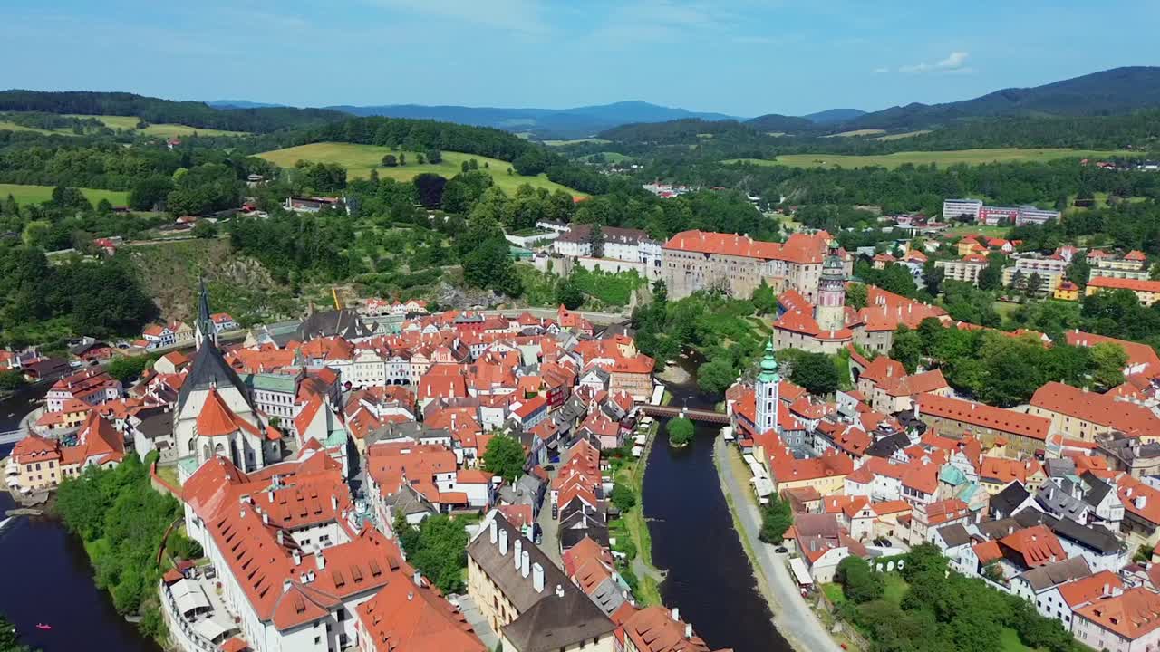 A slow flying down shot over a historic city centre. There are a bunch of old buildings and a castle in the middle. It's a sunny day with some clouds