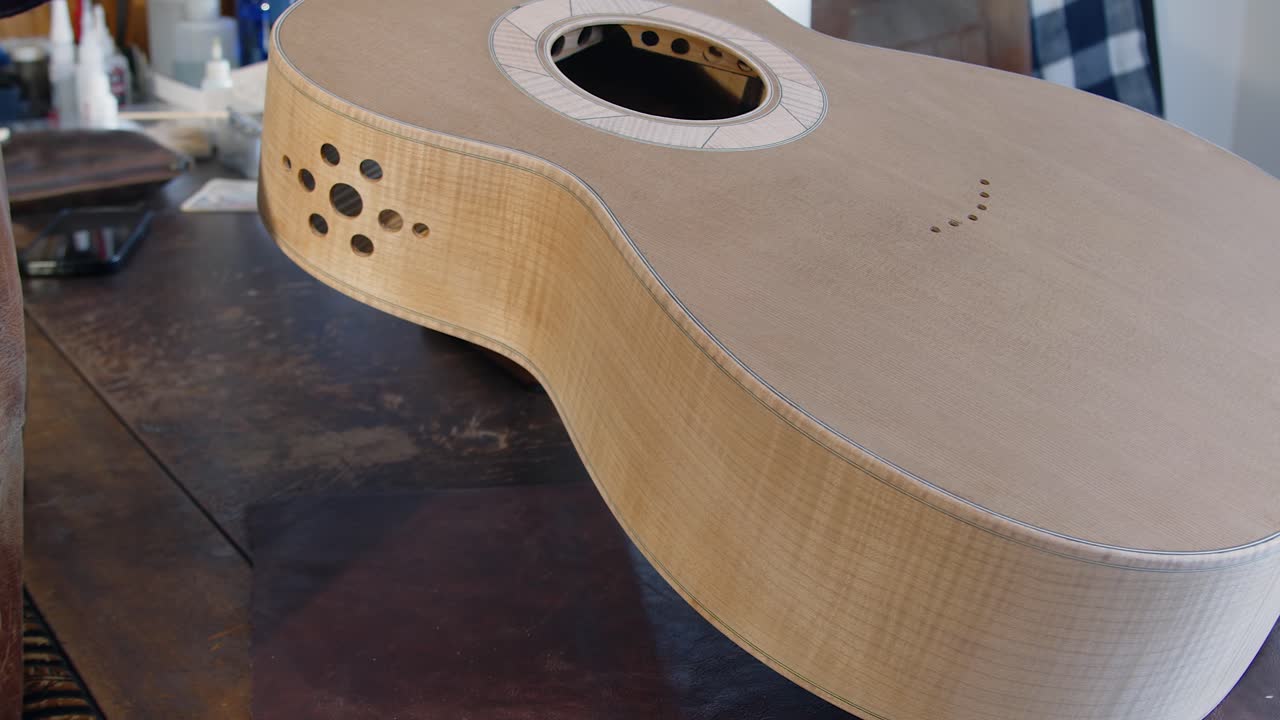 Liutaio mostra la cassa di una chitarra acustica in fase di lavorazione sul banco da lavoro, primo piano.