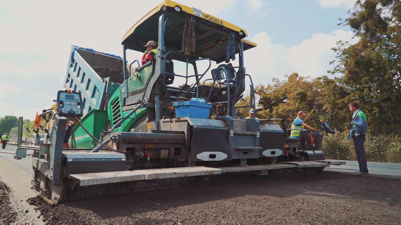 Large asphalt laying machine and team of workers on the road. Asphalt spreader at work in summer. Process of road construction.