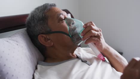 senior mixed race man lying in bed at home using a face mask ventilator