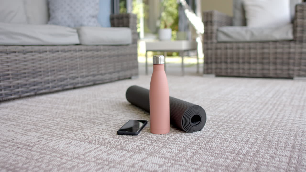 A smartphone and water bottle are resting next to a rolled-up yoga mat