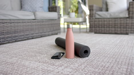 a smartphone and water bottle are resting next to a rolled-up yoga mat