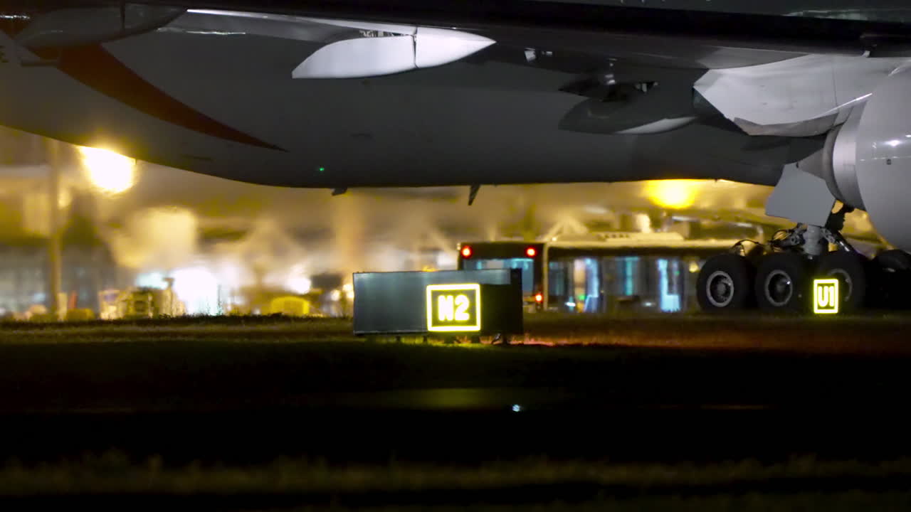 Airplane standing on taxiway with visible landing gear and vehicles at night