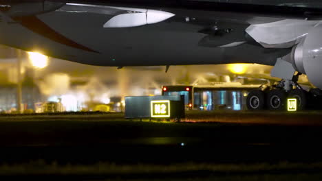 airplane standing on taxiway with visible landing gear and vehicles at night
