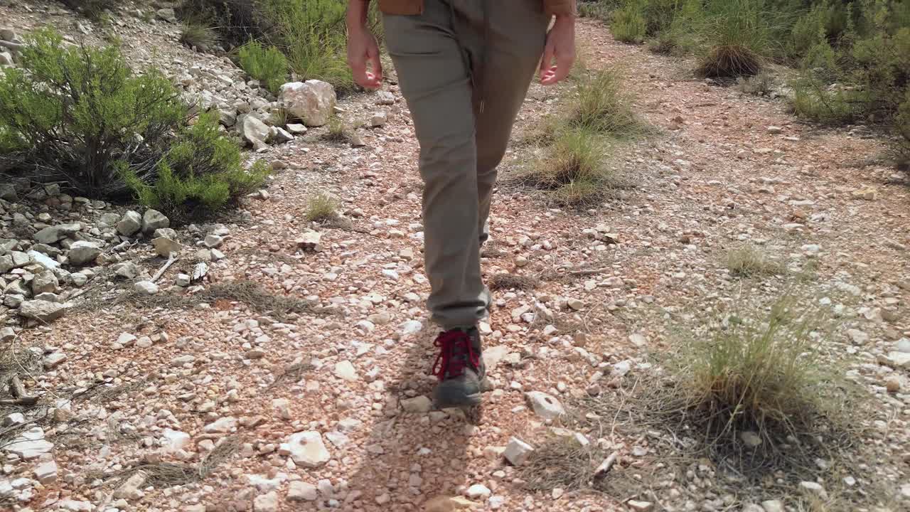 Close-up of a hiker woman's boots walking slowly along a rocky path, surrounded by vegetation
