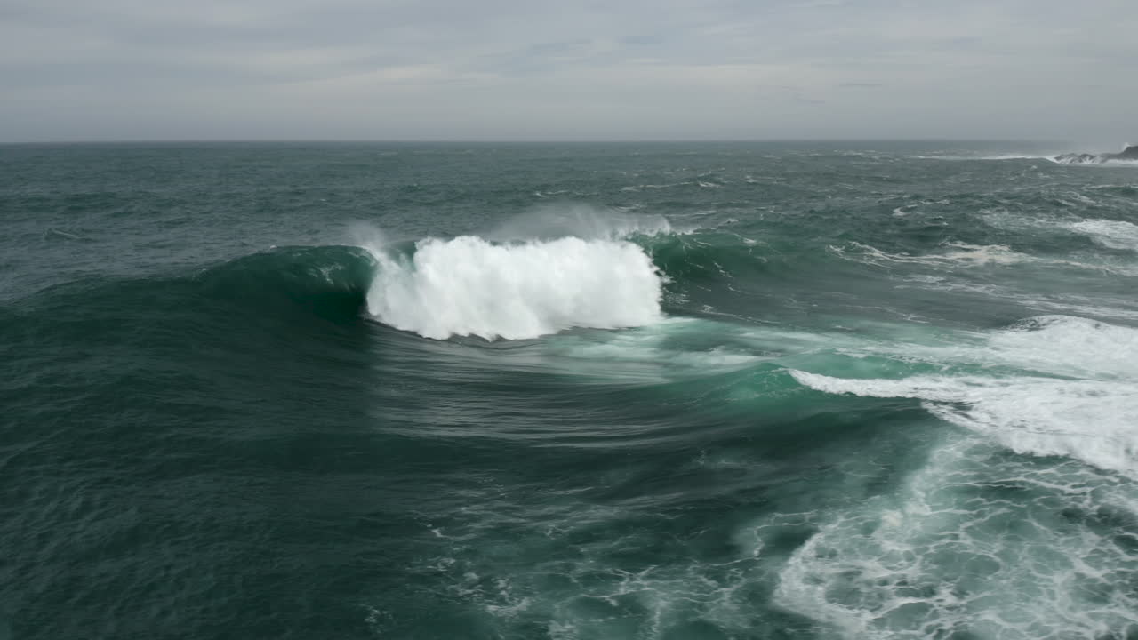 Large wave explodes onto a shallow reef. Aerial shot flying towards the wave and panning around to reveal rocky shoreline.