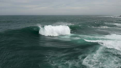 large wave explodes onto a shallow reef. aerial shot flying towards the wave and panning around to reveal rocky shoreline.