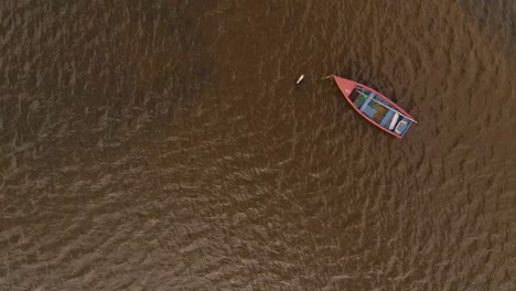 4K-aerial-view-of-small-wooden-boat-moored-in-the-Ria-de-Aveiro,-drone-looking-down-over-the-boat-that-is-moving-slowly-in-the-river-current