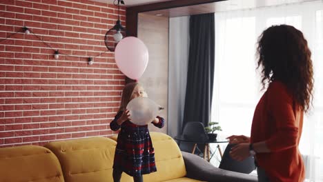 atractiva madre joven y su encantadora hija jugando juntos con globos rosados
