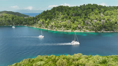 Drone-follow-trucking-shot-of-two-catamaran's-sailing-next-to-the-green-Mljet-island-in-Croatia-on-a-sunny-day