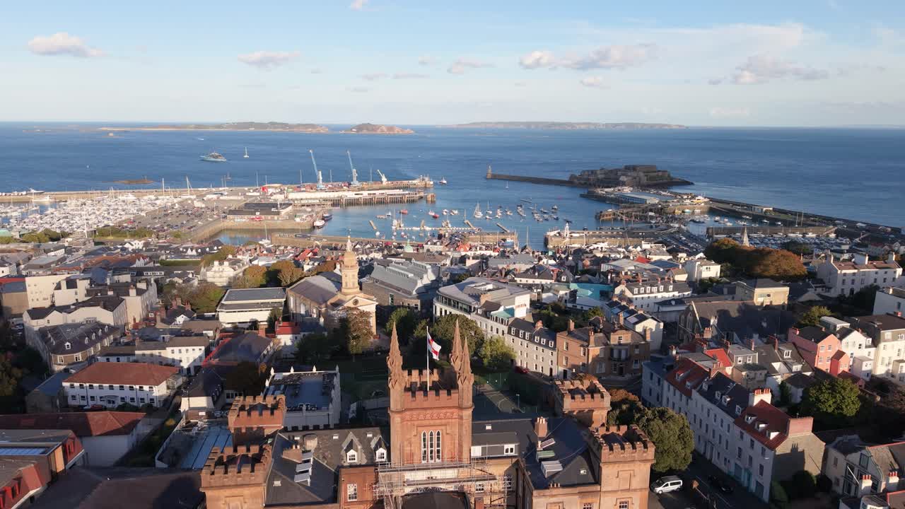 View from Elizabeth College across St James and rooftops of St Peter Port Guernsey towards harbour Herm Sark and Jethou in the distance in bright afternoon sunshine on calm day