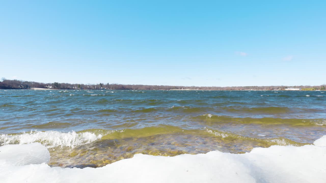 A peaceful winter scene at Lake Ronkonkoma, Long Island. Clear blue skies reflect over shimmering icy waters, creating a tranquil moment of natural beauty. Captures the serene charm of the season.
