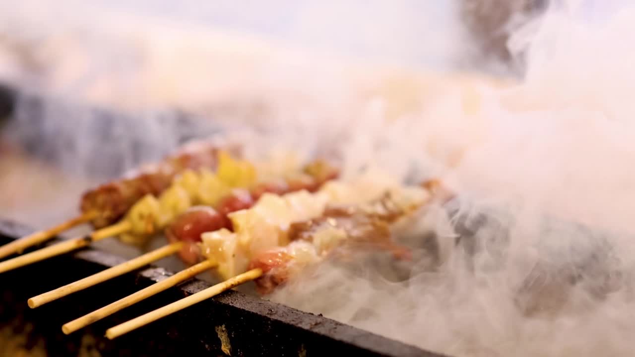 Hands cooking skewered meat over smoky barbecue