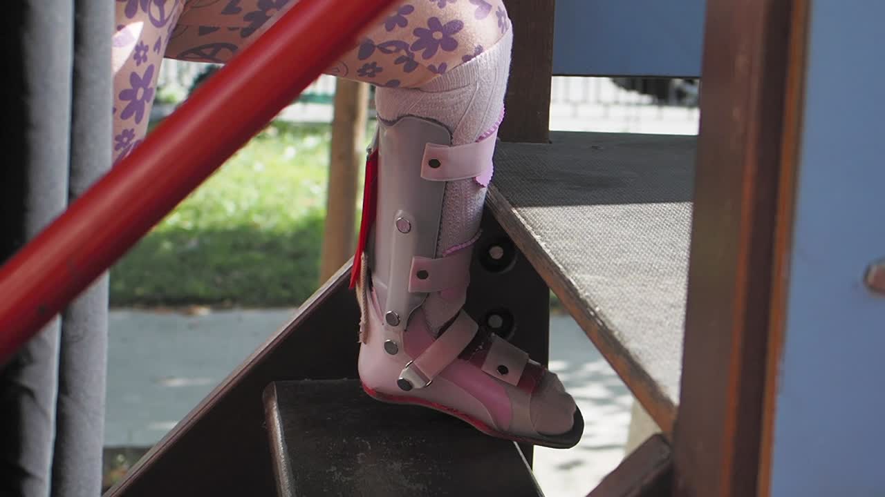 niña con correa en la pierna subiendo las escaleras del patio de recreo