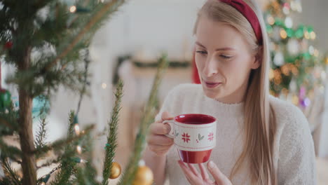 Feliz-Hermosa-Joven-Tomando-Café-Cerca-Del-árbol-De-Navidad-En-Casa