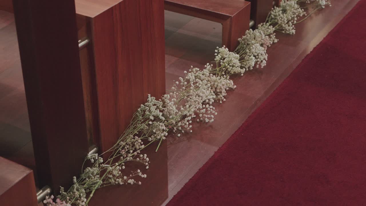 Close view of delicate white flowers adorning wooden pews along a red carpet aisle