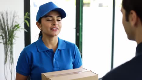 a delivery person wearing a blue cap and shirt smiles while handing a package to a customer at a stylish apartment entrance during the day.