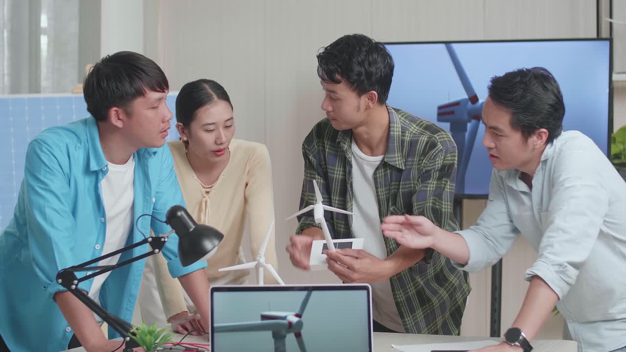 테이블 위의 노트북은 아시아 엔지니어 그룹이 사무실에서 작업에 대해 논의하는 동안 풍력 터빈의 비디오를 보여주고 있습니다.