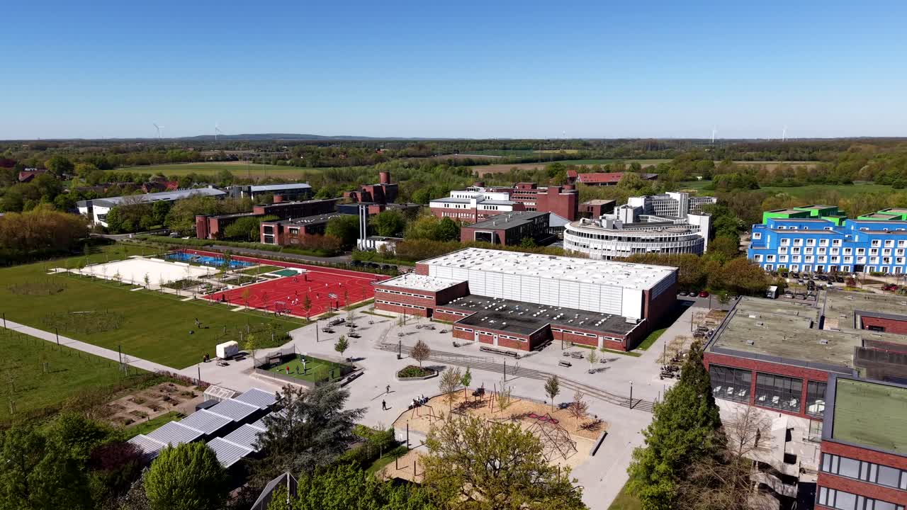 Avvicinamento aereo di un campus universitario in una città americana con campi sportivi e case dormitorio colorate. Giornata di sole in primavera. Piccola città degli USA. Campo lungo. Edificio scolastico con facciata in mattoni rossi.