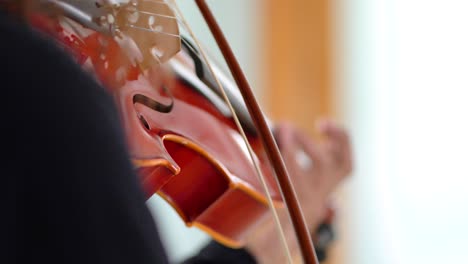 close up of musician's hands rhythmically bowing music on red viola in white studio