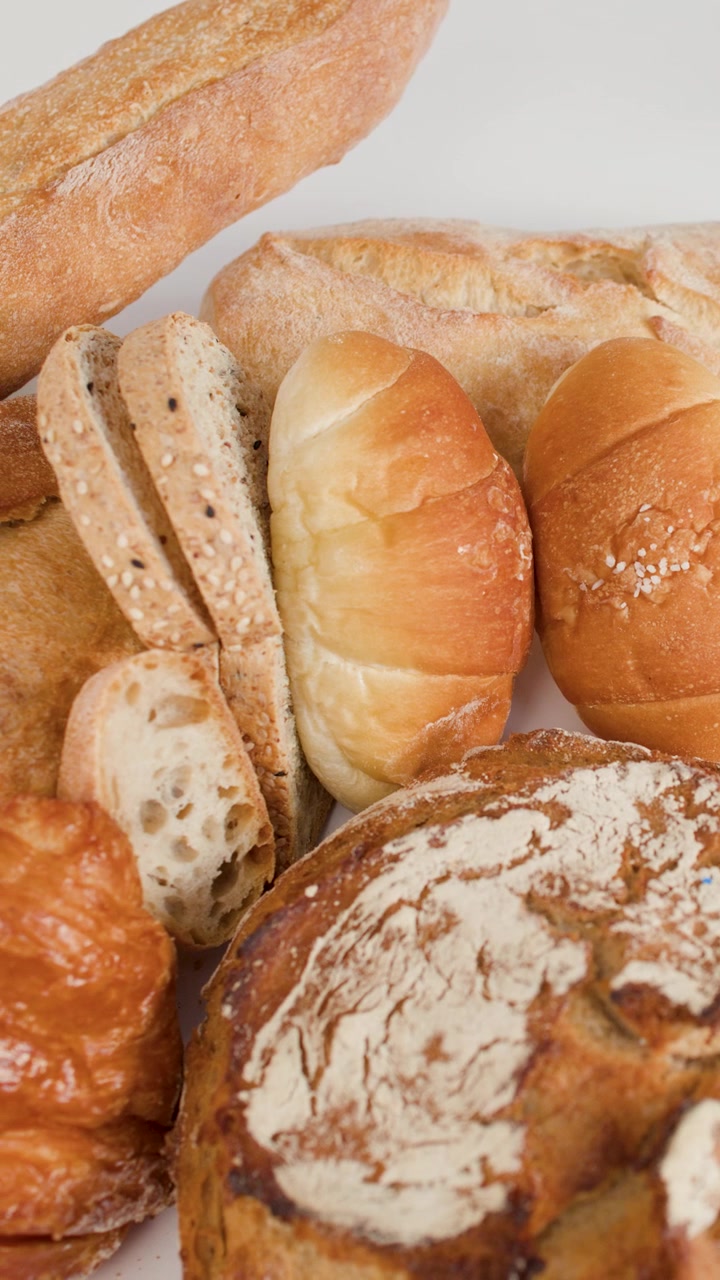 Close-up of hands slicing bread on a wooden board surrounded by various artisan loaves.