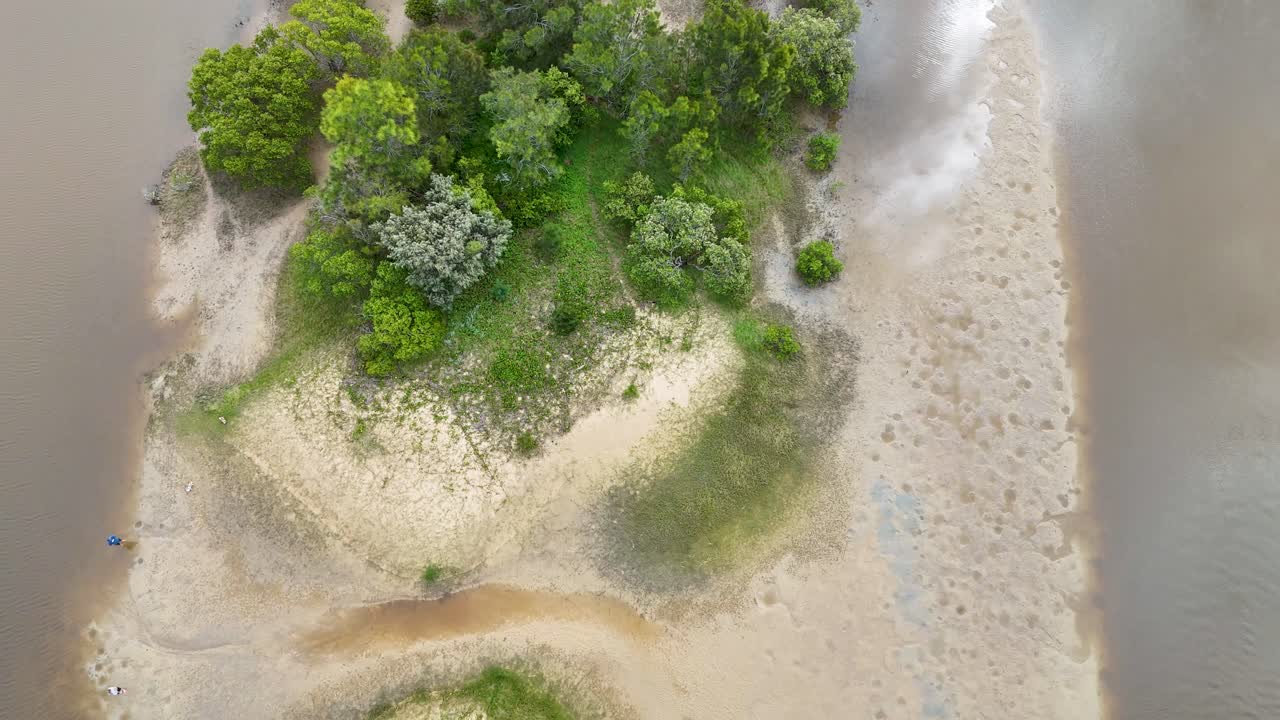 Overhead drone view moves along lush sandspit, estuary, and shoreline in soft daylight