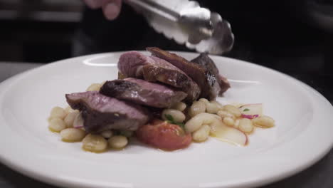 Chef-using-a-knife-to-plate-sliced-beef-and-beans-with-radishes