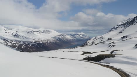 Rising-drone-wide-shot-of-snowy-mountain-landscape-with-road-and-Fjord-in-the-valley