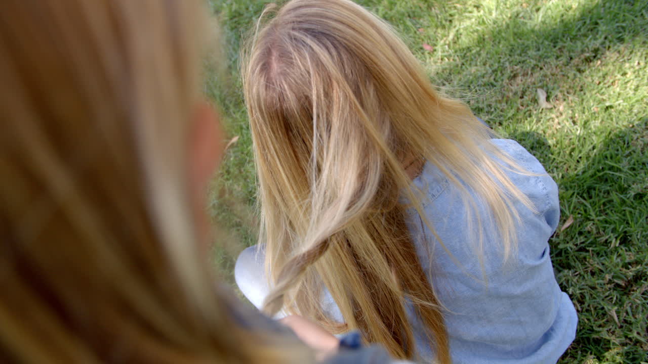 Young girl braiding mother's hair in a park, elevated view