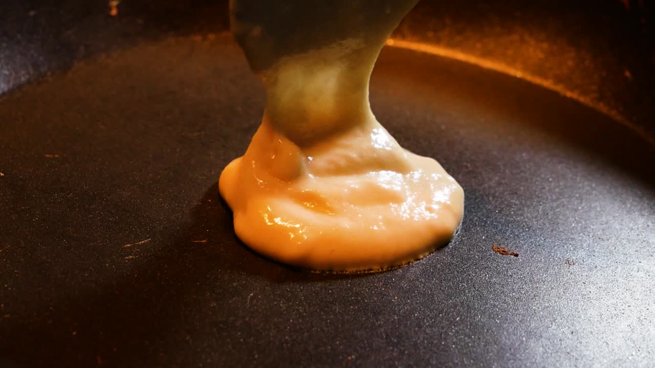 Putting pancake dough in hot black pan for cooking. Homemade cooking concept