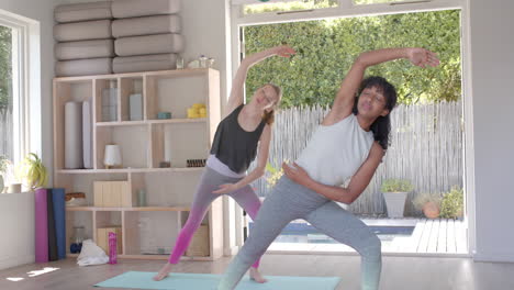 focused diverse fitness women exercising and practicing yoga on mat in white room, slow motion