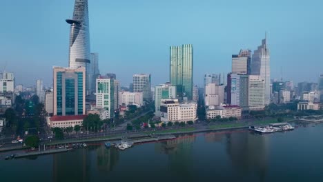 Drone-view-of-District-1-by-Sai-Gon-river-in-Ho-Chi-Minh-city-in-sunrise,-South-Vietnam