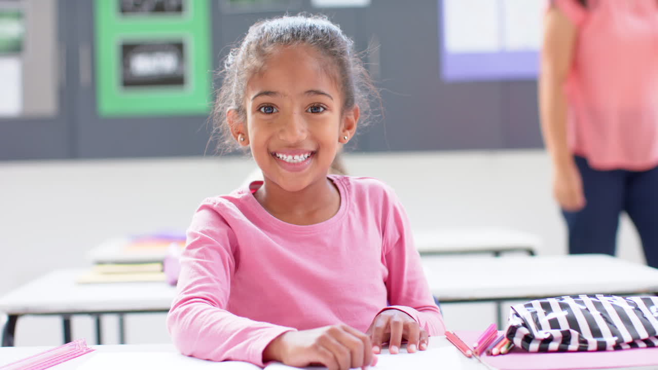 Smiling girl sitting at desk in school classroom with open notebook