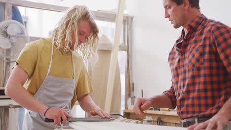 dos fabricantes de tablas de surf masculinos caucásicos trabajando en su estudio y haciendo una tabla de surf de madera juntos