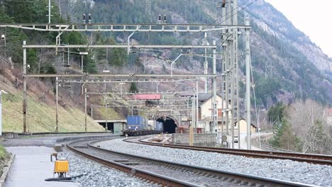 freight train exiting tunnel on mountain track, power lines above, daylight